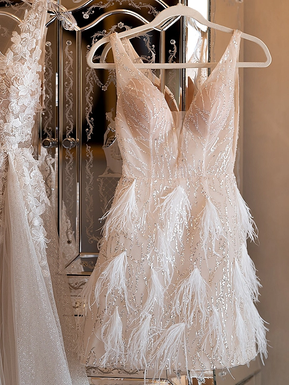 Wedding dress with sequin wedding dress beading and feather hem on a hanger, reflected in a mirrored screen against a beige wall