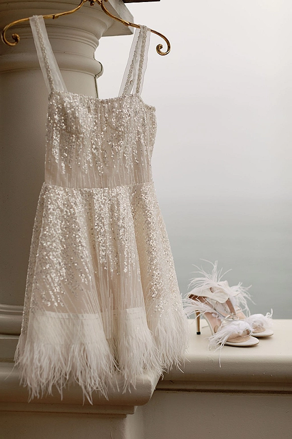 Wedding dress with beaded wedding dress sparkle on a hanger, paired with feather bridal heels on a column pedestal against a neutral wall