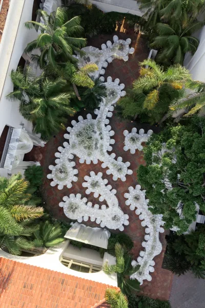 Reception table layout with white floral centerpieces within a palm-lined courtyard with stucco walls and a terracotta roof, framed by greenery.