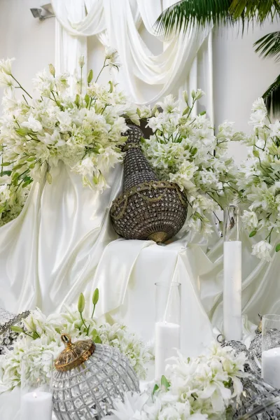 Ceremony decor embraces all white ceremony decor, highlighted by a metallic peacock statue, with palm fronds against a white wall.