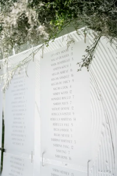 Wedding seating chart with a modern seating chart design on clear acrylic panels, set against a white textured arched backdrop.