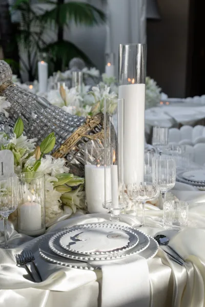 Reception tablescape featuring a white wedding centerpiece of lilies, arranged in a refined monochrome setting with indoor plants behind.