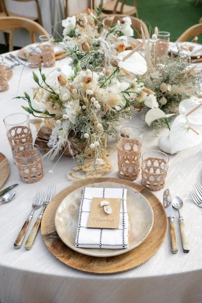 Reception tablescape with neutral wedding table decor, accented by dried florals, set on a grass lawn with wood chairs.