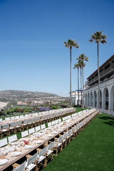 Outdoor reception setup with al fresco reception seating on a lawn with an ocean view and palm trees, tables accented with seashells.