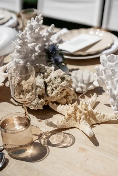 Coastal wedding centerpiece with a starfish accent anchors beach wedding table decor on a sunlit wood tabletop framed by white chairs.