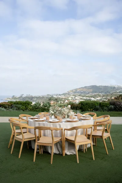 Reception tablescape on a round wedding table featuring amber glassware, overlooking an ocean view on a hillside lawn with succulents.