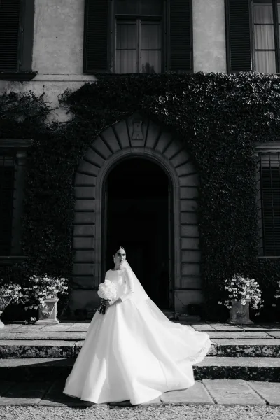 Black-and-white bridal portrait with a cathedral veil, posed before an ivy-covered arched doorway on stone steps