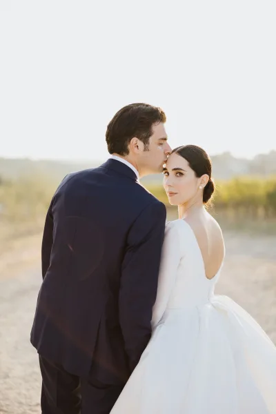 Pearl earrings and a long-sleeved gown stand out as newlyweds embrace for a couple portrait among vineyard vines