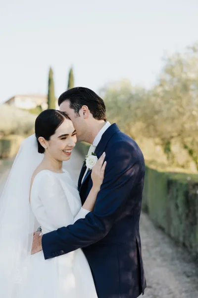 The bride and groom share a forehead kiss in a portrait, with a boatneck gown and white rose boutonniere