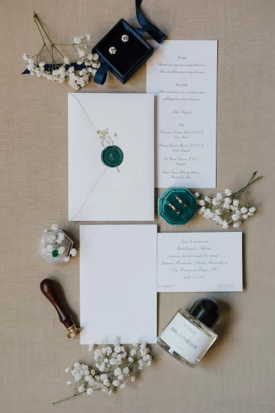 Green wax seal and navy ribbon accompany a wedding invitation suite arranged as a tidy flatlay on linen fabric