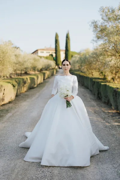 White roses and exposed stems accent a bridal portrait in a satin three-quarter-sleeve gown, framed by manicured hedges