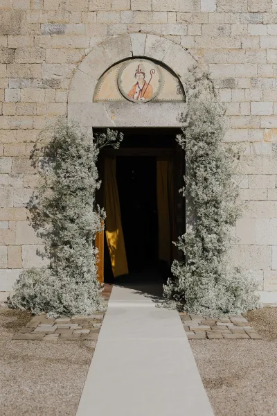 Baby's breath columns flank the ceremony entrance, with a white aisle runner leading toward the draped doorway