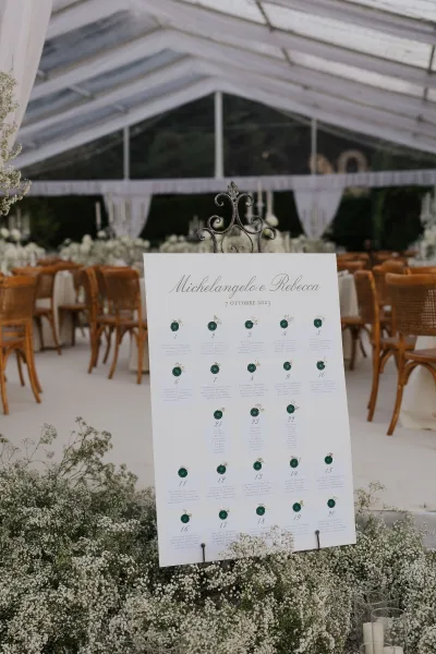 Wax-sealed escort cards accompany a wedding seating chart displayed for guests beneath a clear tent