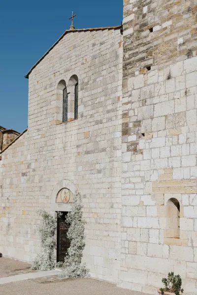White florals and greenery frame the arched entrance of a stone church beside a gravel path