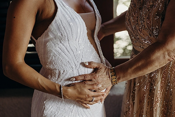 Wedding dress detail with beaded wedding dress bodice, deep V illusion tulle inset, bracelet and ring sparkling in window light indoors