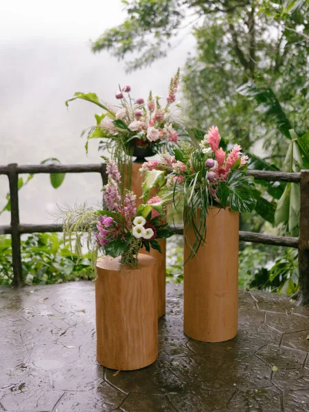 ceremony flowers in lush pedestal flower arrangements with tropical greenery, set against misty forest trees on a stone patio