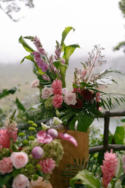 Ceremony flowers forming an altar floral arrangement with orchids, framed by garden foliage and a wooden railing under a foggy sky.