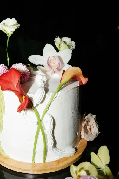 Wedding cake styled as a floral wedding cake, adorned with a single white orchid, set against a black backdrop on a glass tabletop.
