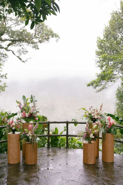 Wedding altar with outdoor ceremony decor in tropical foliage, set on a stone terrace facing forest trees and a misty valley.
