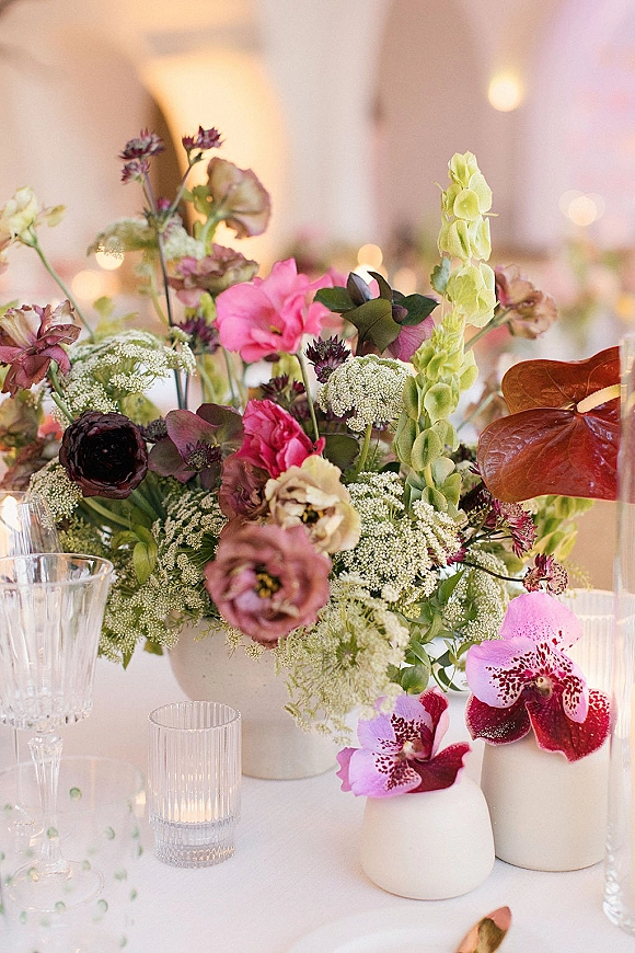 Wedding centerpieces with a floral centerpiece of orchids and mixed flowers in white ceramic vases on a tented table under string lights