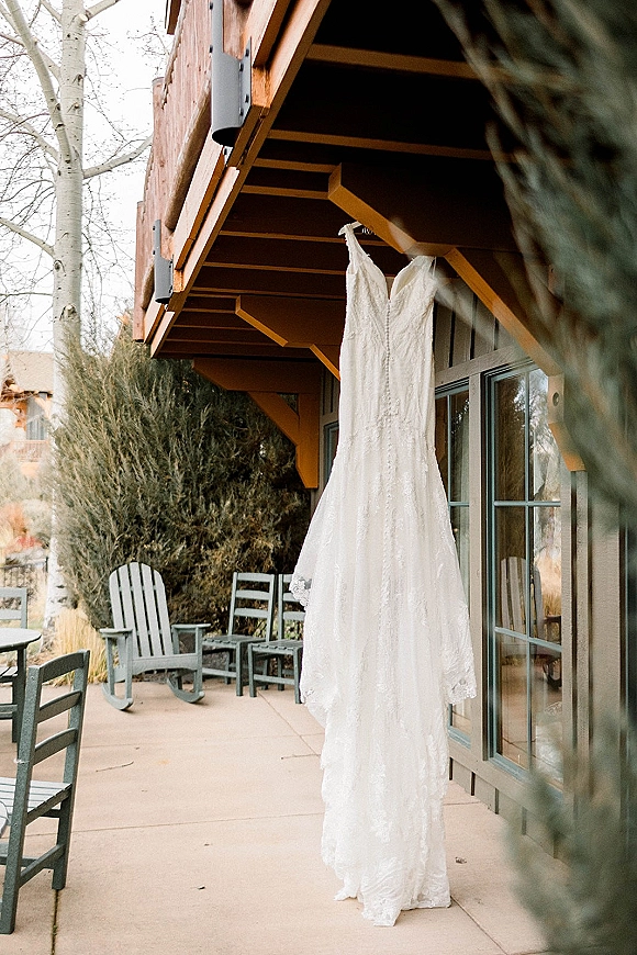 Wedding dress with lace wedding dress detailing, V-neck and spaghetti straps, hanging on a wooden porch outside a house in natural light
