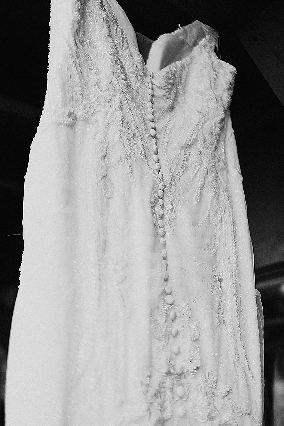 Wedding dress with lace wedding dress details, sheer illusion bodice and fabric-covered buttons, hanging in a dark interior setting