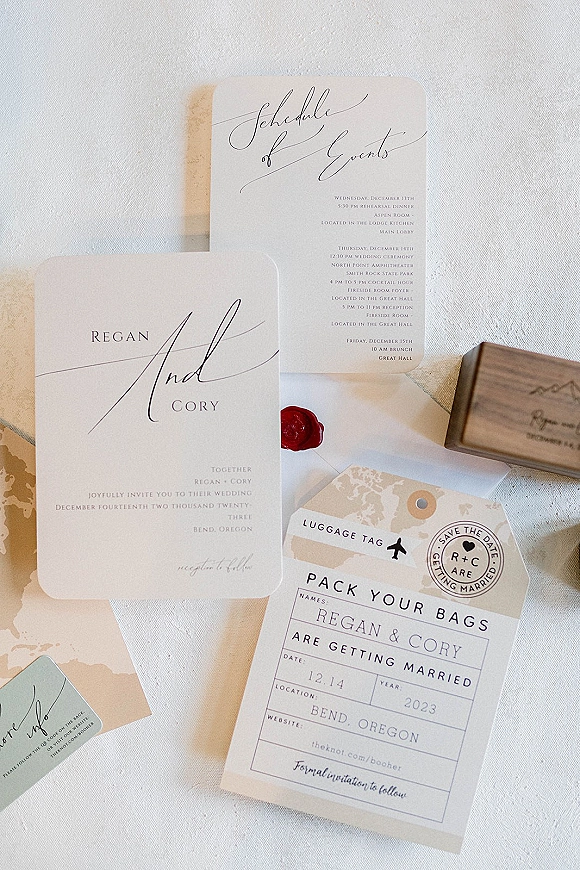 Invitation suite with wedding invitation suite cards, envelopes and red wax seal, plus map paper and wooden stamp on white linen flat lay