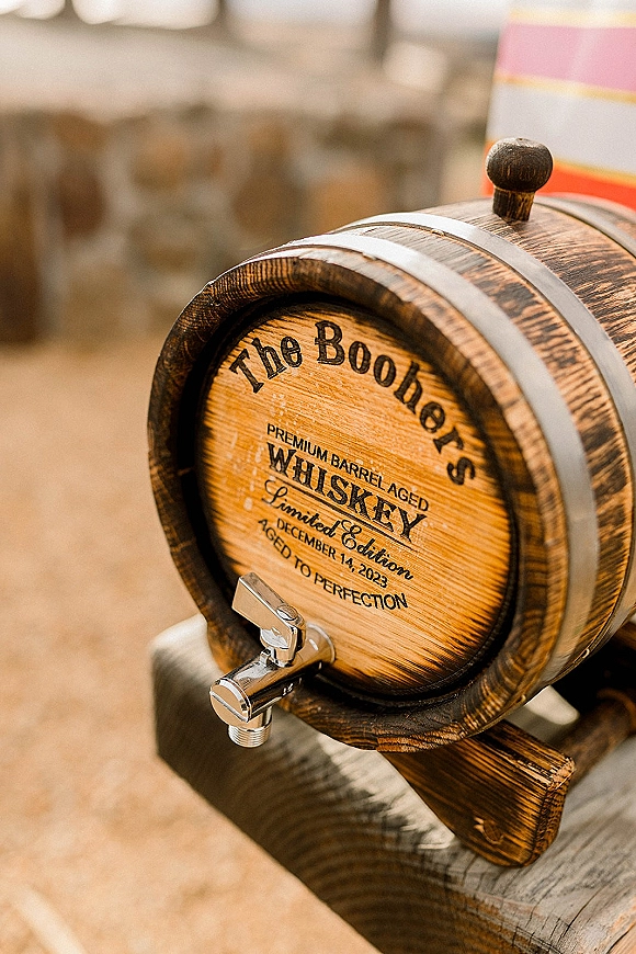 Whiskey barrel guest book with engraved whiskey barrel label, metal spigot and hoops on a stand atop a wood tabletop in soft indoor blur