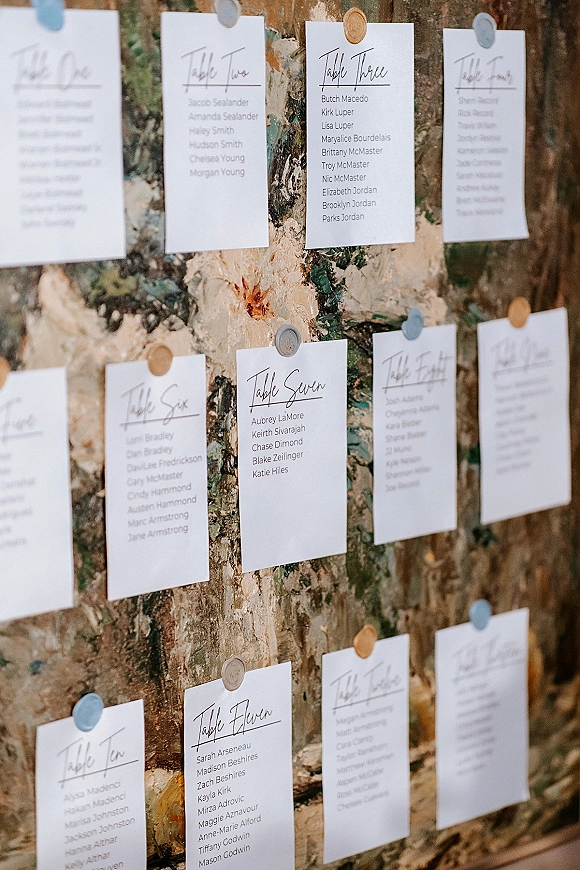 Wedding seating chart with seating chart cards pinned by push pins and wax seals on a painted canvas backdrop indoors