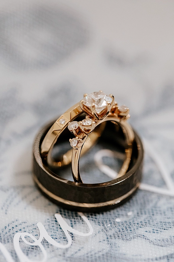 Wedding rings with a diamond engagement ring and black wedding band, arranged on a marble surface beside a calligraphy card