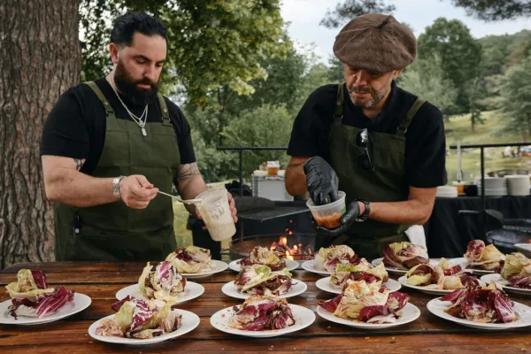 Wedding catering at an outdoor catering station as chefs plate salads by an open flame during service.