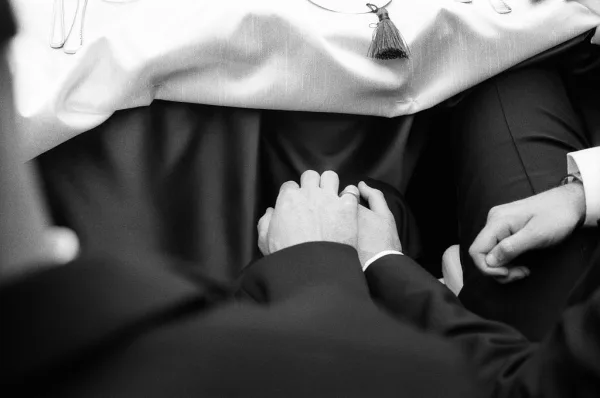 Couple holding hands in a tender reception table moment, their wedding rings catching light as fingers lace in a quiet, candid pause.