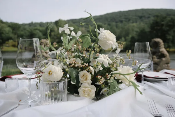 Wedding centerpiece, a white rose centerpiece with greenery, accented by a burgundy napkin on a lakeside reception table.