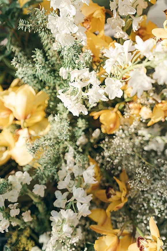 Wedding bouquet with yellow wedding bouquet tones, white flowers, greenery and baby’s breath, shot close up against blurred florals