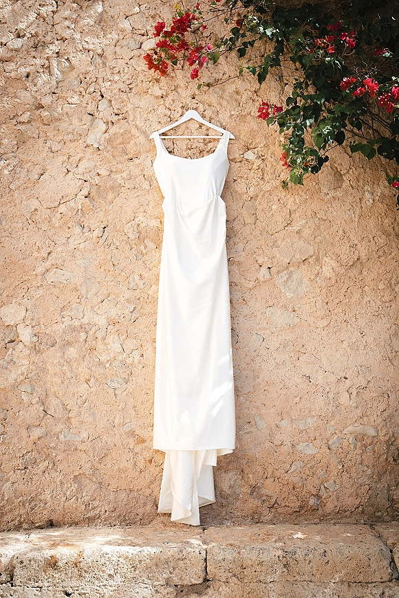 Wedding dress and simple wedding dress hanging on a dress hanger against a stone wall with bougainvillea vine by outdoor steps