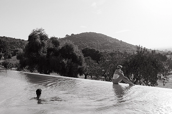 Couple in pool during a wedding weekend pool day, wearing swimsuits and sunglasses in an infinity pool with hills and trees beyond