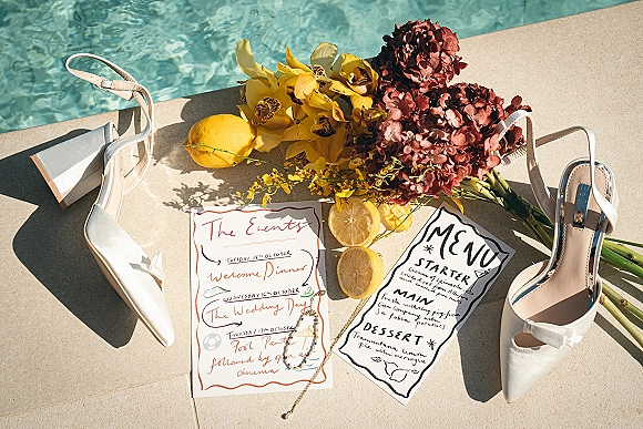 Wedding invitation suite with calligraphy wedding invitations, menu and event cards, styled with white heels, lemons, and orchids by a poolside deck