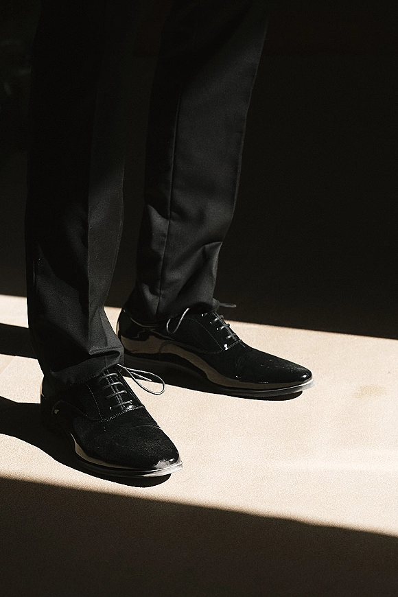 Groom shoes, black wedding shoes men, neatly laced under black suit trousers on a light floor with soft shadow and dark backdrop