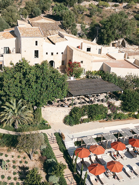 Wedding venue exterior at a mediterranean wedding venue with white stucco villa, terracotta roof tiles, pergola dining patio, and hillside gardens