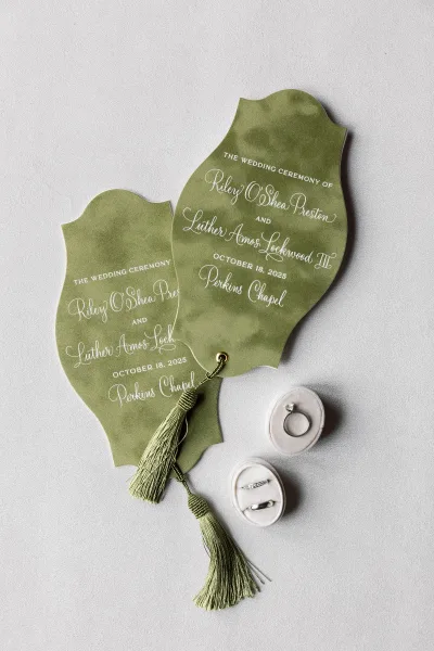 Wedding invitation suite with green wedding invitations, die-cut calligraphy cards and ring boxes arranged on a light gray surface
