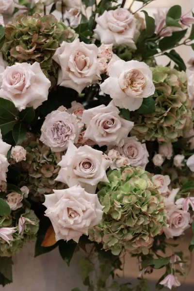 Wedding floral arrangement featuring blush roses and hydrangea blooms with greenery and pink buds against a neutral wall backdrop