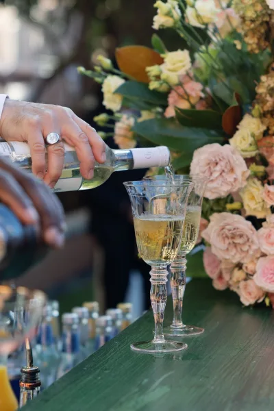 Wedding bar drinks with a white wine bottle and glasses on the bar counter, accented by roses and greenery against a blurred bar setup