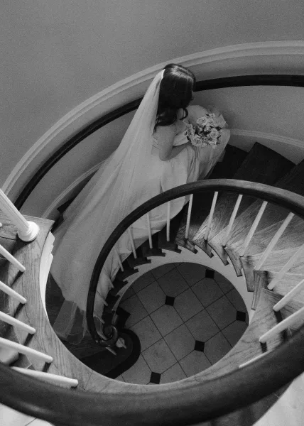 Bridal portrait of a bride holding bouquet on a spiral staircase, long veil trailing down the stairs beside her wedding dress