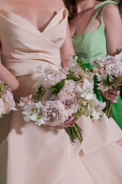 Bridesmaid bouquets of pastel bridesmaid bouquets in blush roses, white florals, and greenery against a neutral indoor backdrop in soft light