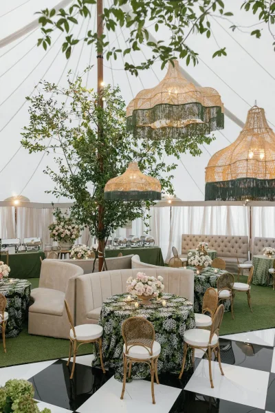 Reception tablescape with green floral tablecloth wedding decor, candles and centerpieces under a clear top tent with string lights and checkered dance floor