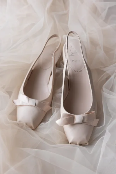 Bridal shoes, ivory wedding heels with satin bow on slingback pointed toes, styled on soft tulle fabric against a neutral backdrop