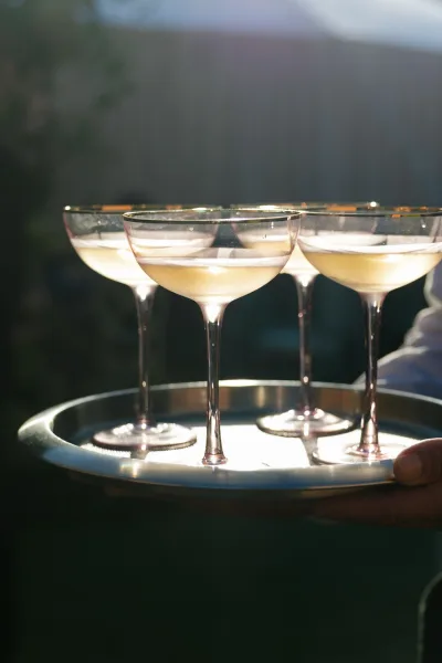 Champagne coupe toast with champagne coupe glasses on a serving tray in warm sunlight, creating a sparkling outdoor wedding cocktail moment