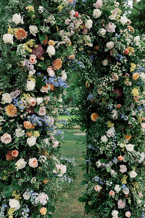 Floral ceremony arch with garden wedding arch flowers in roses, dahlias, wildflowers and greenery on a lawn beneath garden trees