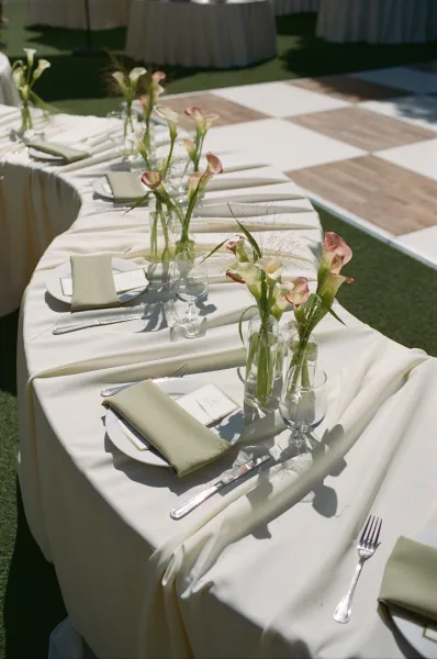 Reception tablescape for a sage green wedding table with elegant calla lilies, set on a grass lawn beside the dance floor.