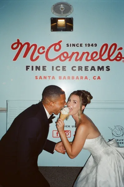 Couple portrait of a bride and groom sharing ice cream, the bride holding an ice cream cone beside an ice cream truck with logo signage.
